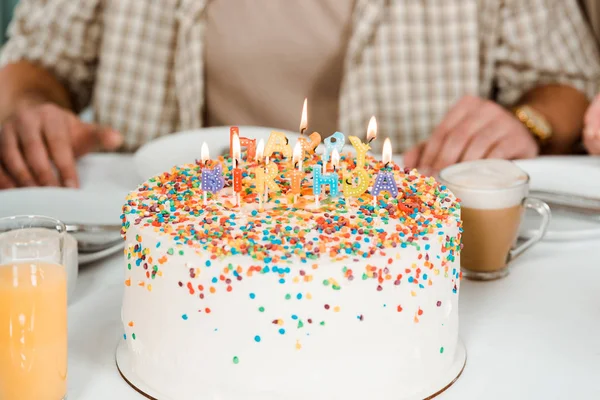 Cropped view of man sitting near birthday cake with colorful burning candles — Stock Photo