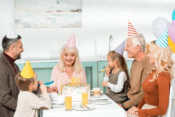 Mulher sênior feliz olhando para bolo de aniversário enquanto sentado na mesa servida com a família — Fotografia de Stock