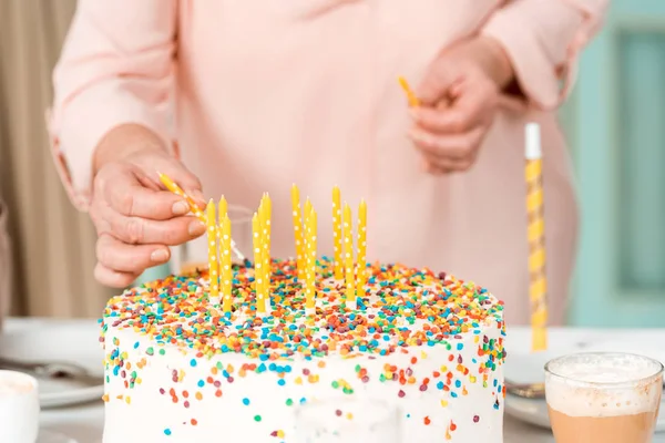 Cropped view of senior woman putting candles in delicious birthday cake — Stock Photo