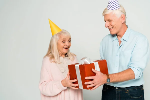 Allegro marito anziano e moglie in possesso di scatola regalo rossa isolato su grigio — Foto stock