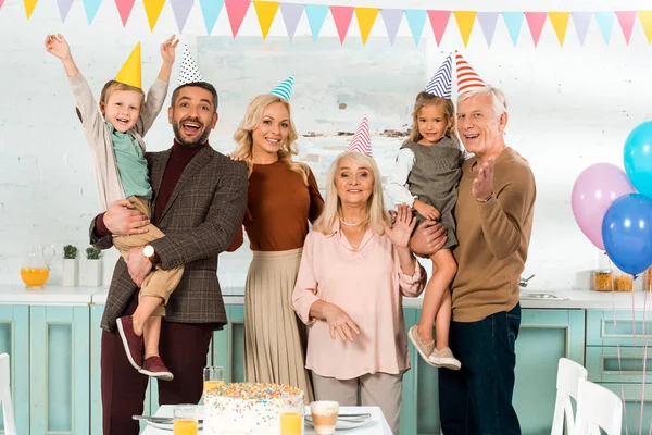 Famiglia felice in piedi vicino al tavolo della cucina con torta di compleanno e guardando la fotocamera — Foto stock