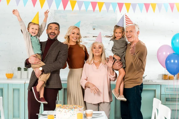 Happy family standing near kitchen table with birthday cake and looking at camera — Stock Photo