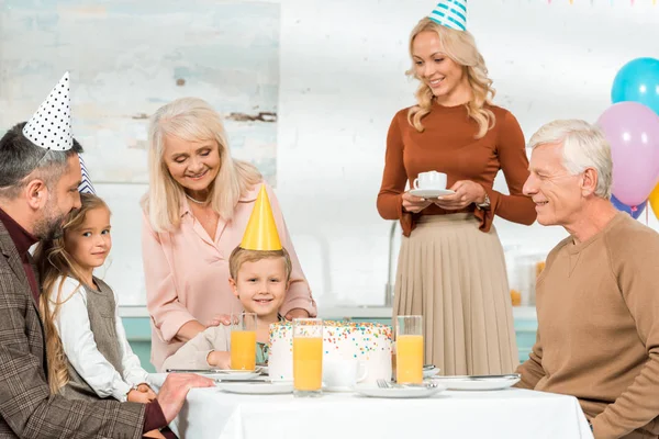 Glückliche Familie sitzt am servierten Küchentisch mit Geburtstagstorte — Stockfoto