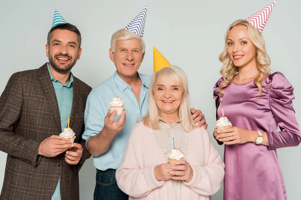 Happy senior parents with adult children holding birthday cupcakes isolated on grey — Stock Photo