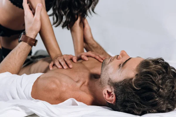 Обрезанный вид сексуальной женщины над безрубашечным мужчиной лежащим на кровати — стоковое фото