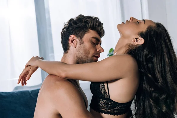 Séduisante fille en soutien-gorge noir embrassant homme torse nu avec les yeux fermés — Photo de stock