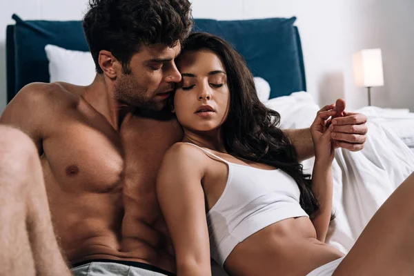 Sexy hombre de la mano de seductora novia mientras está sentado en la cama - foto de stock