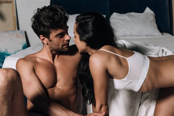 Bello, muscoloso uomo guardando sexy fidanzata a letto — Foto stock