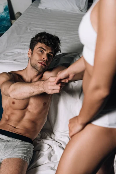 Sexy homme en sous-vêtements couché dans le lit et tenant la main de petite amie — Photo de stock