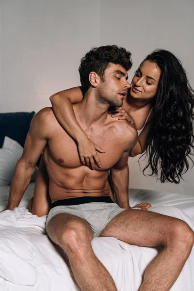 Lächelndes, sinnliches Mädchen umarmt sexy, hemdlosen Freund im Schlafzimmer — Stockfoto
