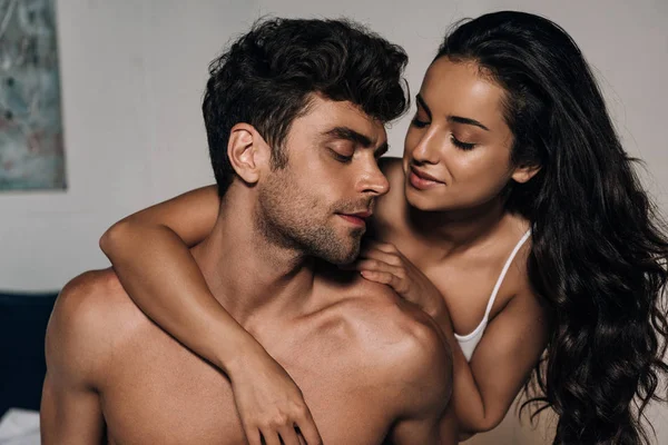 Menina atraente abraçando namorado sem camisa no quarto — Fotografia de Stock