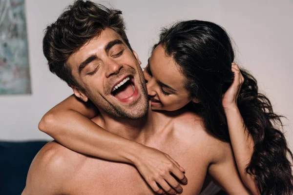 Happy woman biting neck of cheerful boyfriend in bedroom — Stock Photo