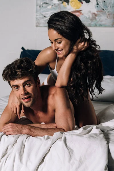Fröhlicher Mann blickt in die Kamera, während er mit glücklicher Freundin im Bett liegt — Stockfoto