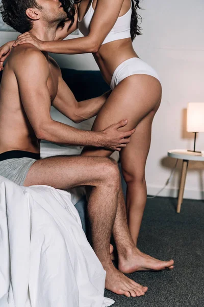 Vista ritagliata di ragazza sexy in lingerie e fidanzato seduto sul letto e abbracciarla — Foto stock