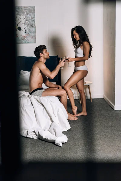 Selective focus of sexy couple in underwear clinking glasses of red wine in bedroom — Stock Photo