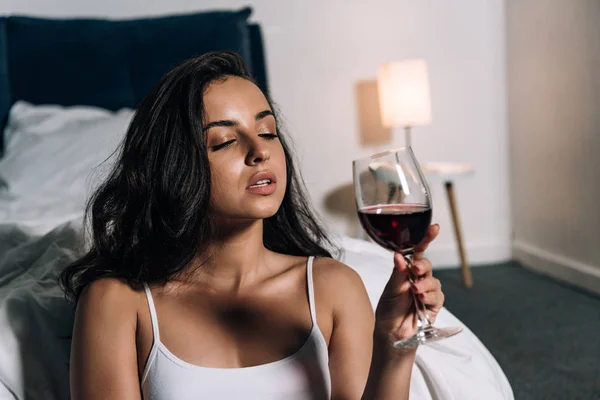 Sensual, dreamy girl holding glass of red wine in bedroom — Stock Photo