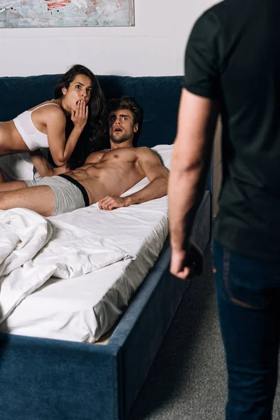 Mulher chocada e seu amante olhando para o marido de pé perto da cama — Fotografia de Stock
