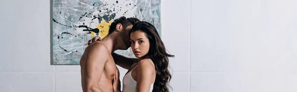 Panoramic shot of attractive girl looking at camera while shirtless man kissing her — Stock Photo