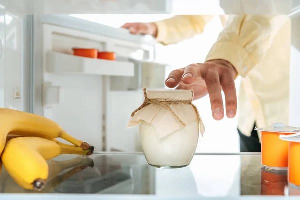 Abgeschnittene Ansicht eines Mannes, der saure Sahne aus dem offenen Kühlschrank nimmt, isoliert auf weiß — Stockfoto