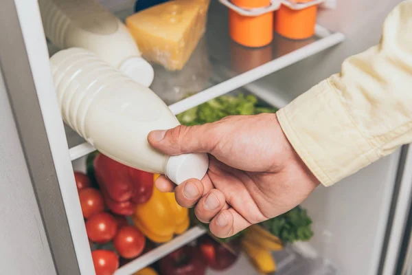 Обрезанный вид человека, вынимающего бутылку молока из холодильника — стоковое фото