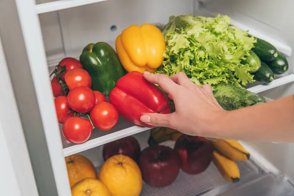 Vista recortada de la mujer sacando pimiento de la nevera con verduras y frutas frescas - foto de stock