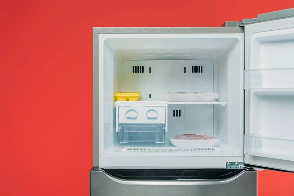 Frozen meat and ice in open freezer isolated on red — Stock Photo