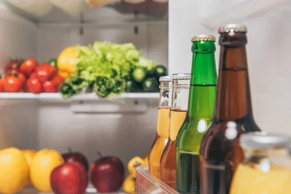 Selective focus of bottles of beer on fridge door near fresh food on shelves — Stock Photo