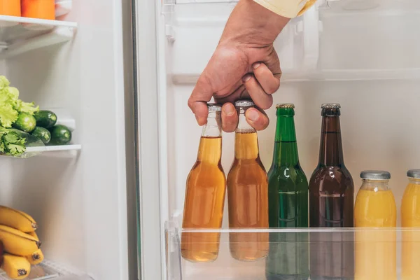 Ausgeschnittene Ansicht eines Mannes, der Bierflaschen aus dem offenen Kühlschrank mit frischen Lebensmitteln aus den Regalen holt — Stockfoto