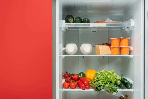 Open fridge full of fresh food on shelves isolated on red — Stock Photo