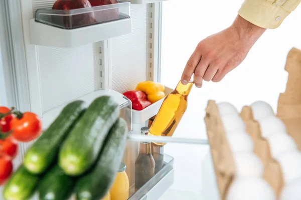 Cropped view of man taking bottle of beer out from fridge with fresh food on shelves isolated on white — Stock Photo