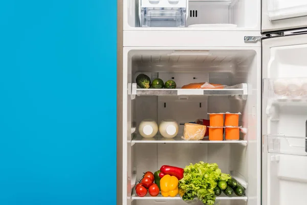 Frigorífico aberto cheio de alimentos frescos em prateleiras isoladas em azul — Fotografia de Stock