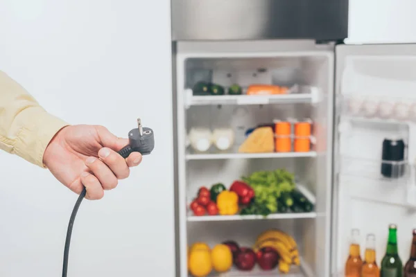 Vista recortada del hombre que sostiene el cable de alimentación desenchufado de la nevera aislado en blanco - foto de stock