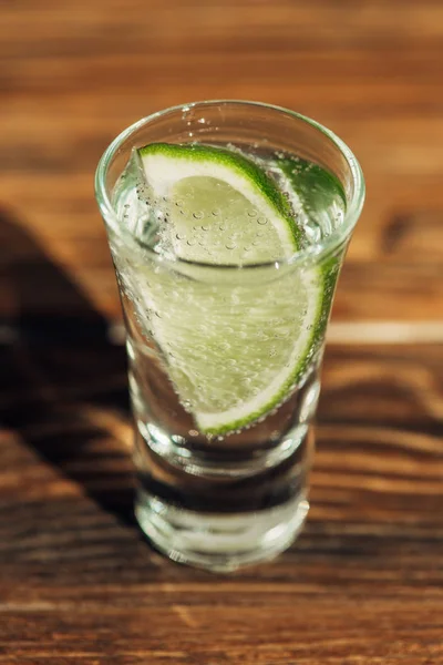 Vista de perto da tequila fresca com limão na superfície de madeira sob a luz solar — Fotografia de Stock