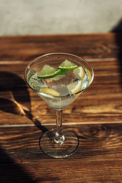 Verre de margarita avec glace, citron et citron vert décoré avec du sucre sur la surface en bois à la lumière du soleil — Photo de stock