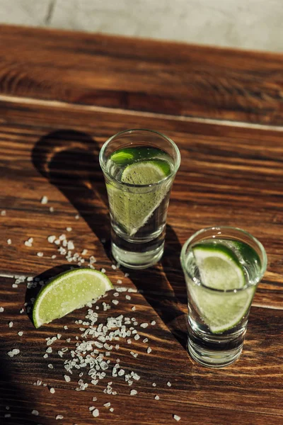 Fresh tequila with lime and salt on wooden surface in sunlight — Stock Photo