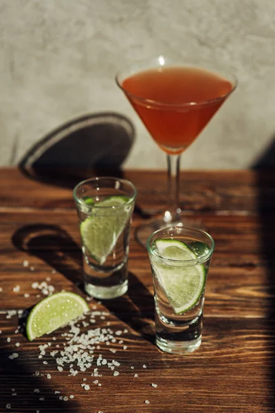 Selective focus of fresh tequila with lime and salt and cocktail on wooden surface in sunlight — Stock Photo