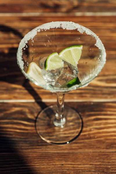 Vaso de martini con hielo, limón y lima decorado con azúcar en la superficie de madera a la luz del sol — Stock Photo