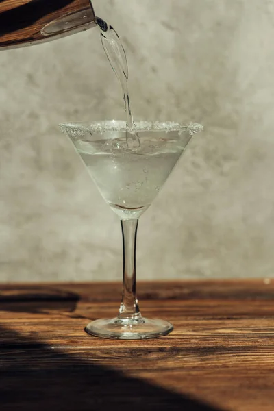 Flüssigkeit aus dem Shaker in Martini-Glas gießen, das mit Zucker auf einer Holzoberfläche im Sonnenlicht dekoriert ist — Stockfoto