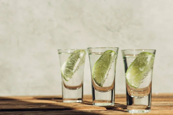 Messa a fuoco selettiva di tequila fresca con calce sulla superficie di legno alla luce del sole — Foto stock