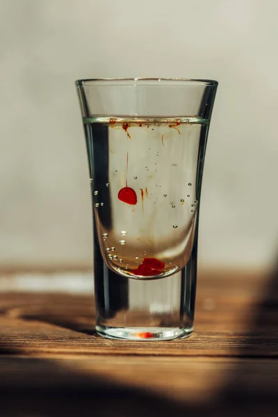 Vue rapprochée du plan avec liquide transparent et rouge sur la surface en bois à la lumière du soleil — Photo de stock