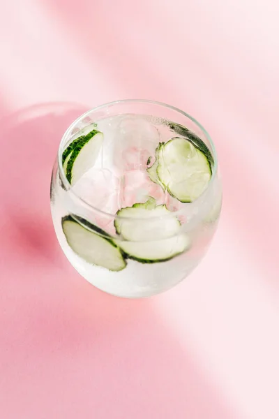Свіжий лимонад з льодом та шматочками огірка на рожевому фоні з сонячним світлом — стокове фото