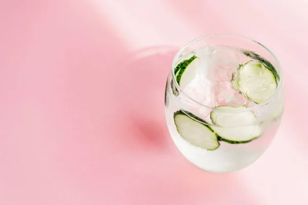 Fresh lemonade with ice and cucumber slices on pink background with sunlight — Stock Photo