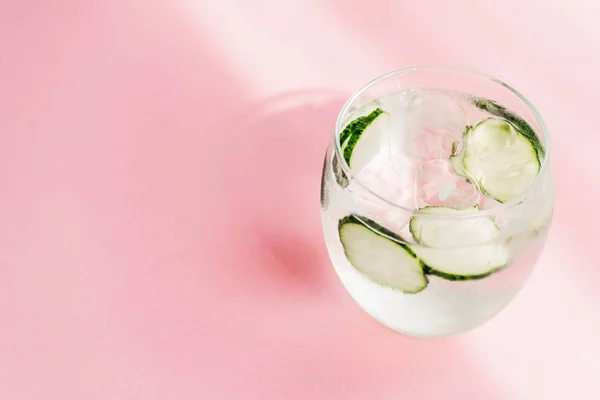 Limonada fresca com gelo e fatias de pepino no fundo rosa com luz solar — Fotografia de Stock