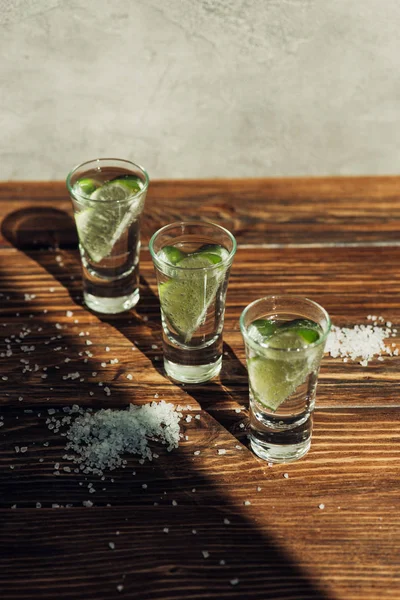 Tequila fresca com limão e sal na superfície de madeira sob a luz solar — Fotografia de Stock