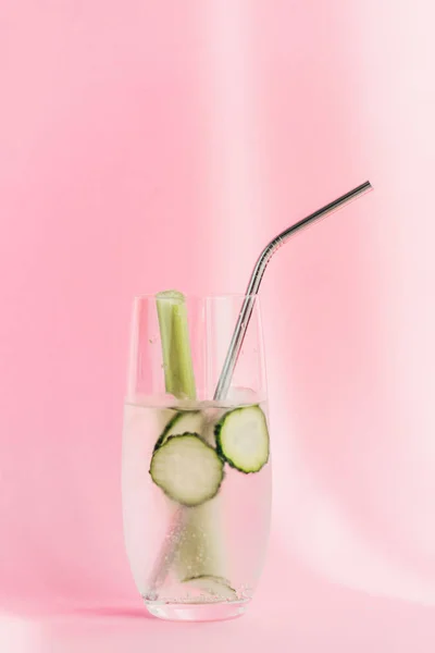 Fresh lemonade with ice, celery, straw and cucumber slices in sunlight on pink background — Stock Photo