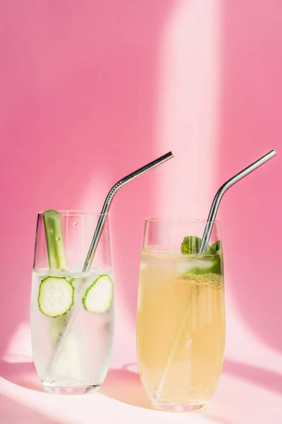 Fresh lemonade in glasses with mint, ice, celery, straws and cucumber slices in sunlight on pink background — Stock Photo