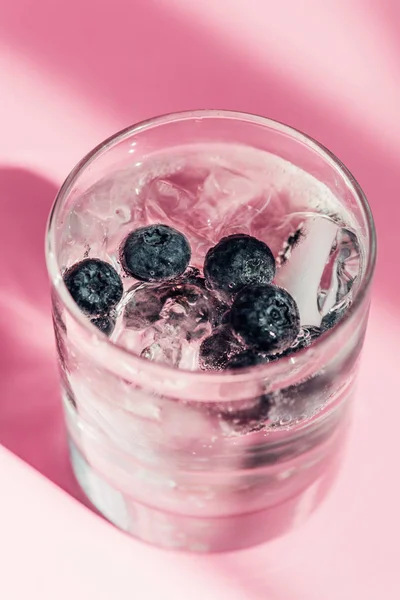 Fresh lemonade with ice and blueberries in sunlight on pink background — Stock Photo