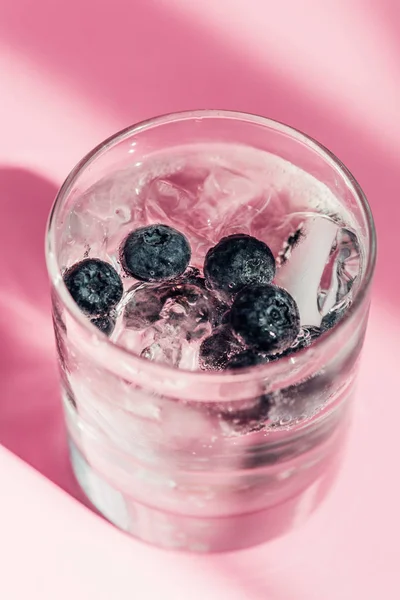 Limonada fresca com gelo e mirtilos à luz solar sobre fundo rosa — Fotografia de Stock