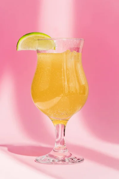 Fresh yellow lemonade with lime slice in sunlight on pink background — Stock Photo
