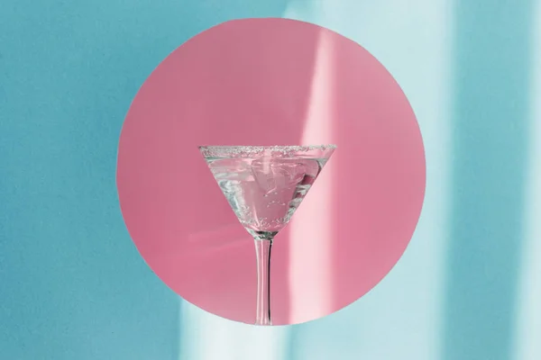 Gin tonic en cristal de martini en círculo rosa sobre fondo azul a la luz del sol - foto de stock